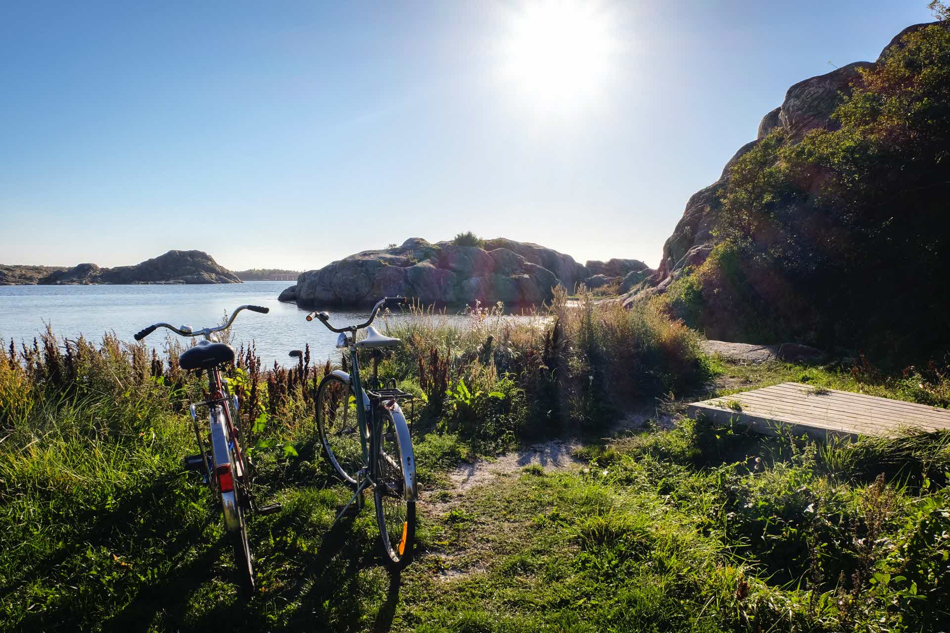 Två cyklar parkerade vid en rastplats intill klippor och vatten.