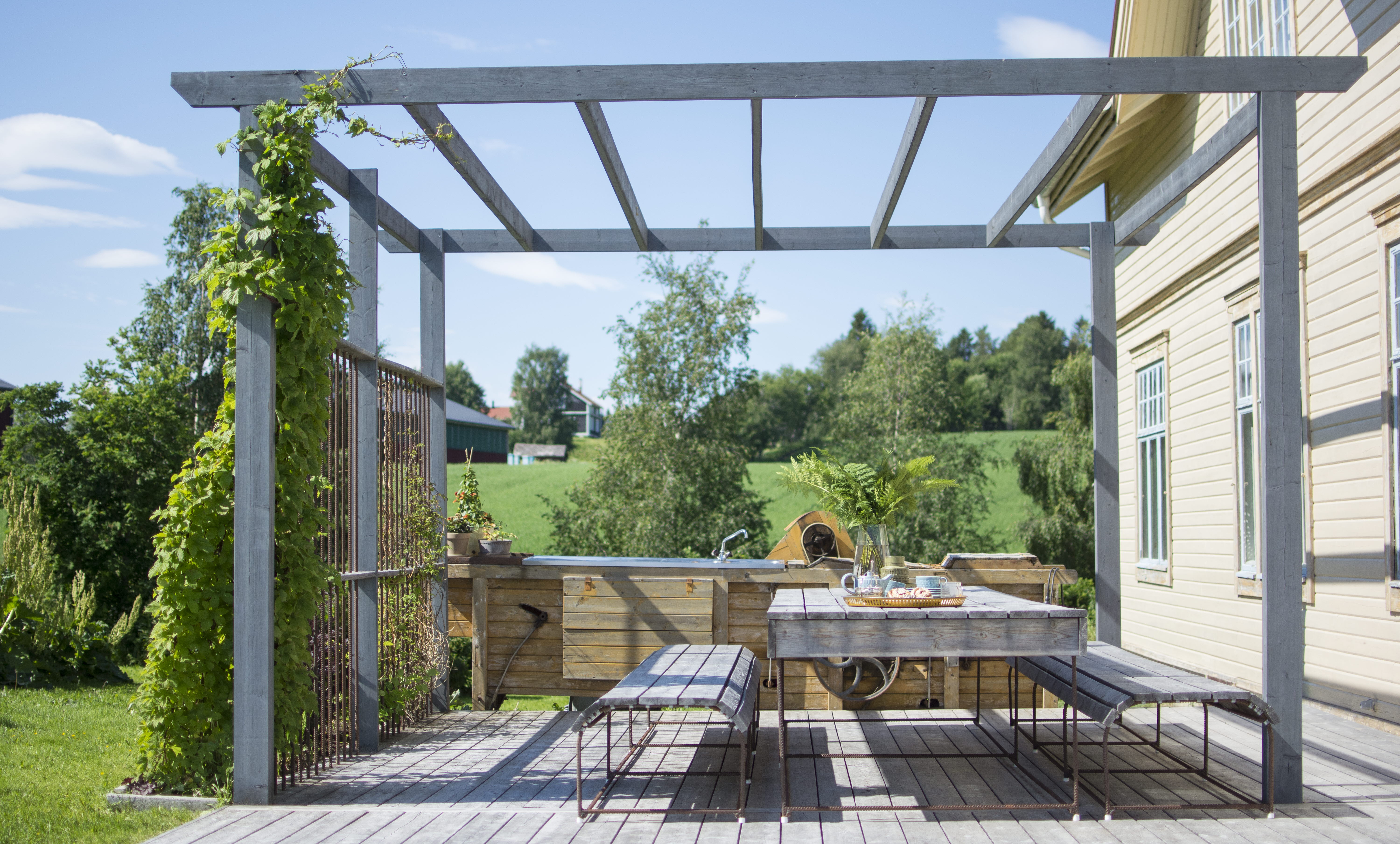 En uteplass med et bord, en sofa og en terrasse, alle bygget i malmfuru.