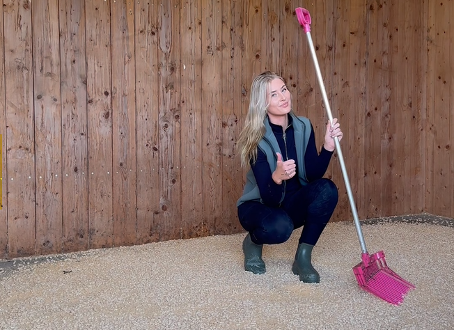 Amy har lagt in Stallpellets i boxen och visar tumme upp