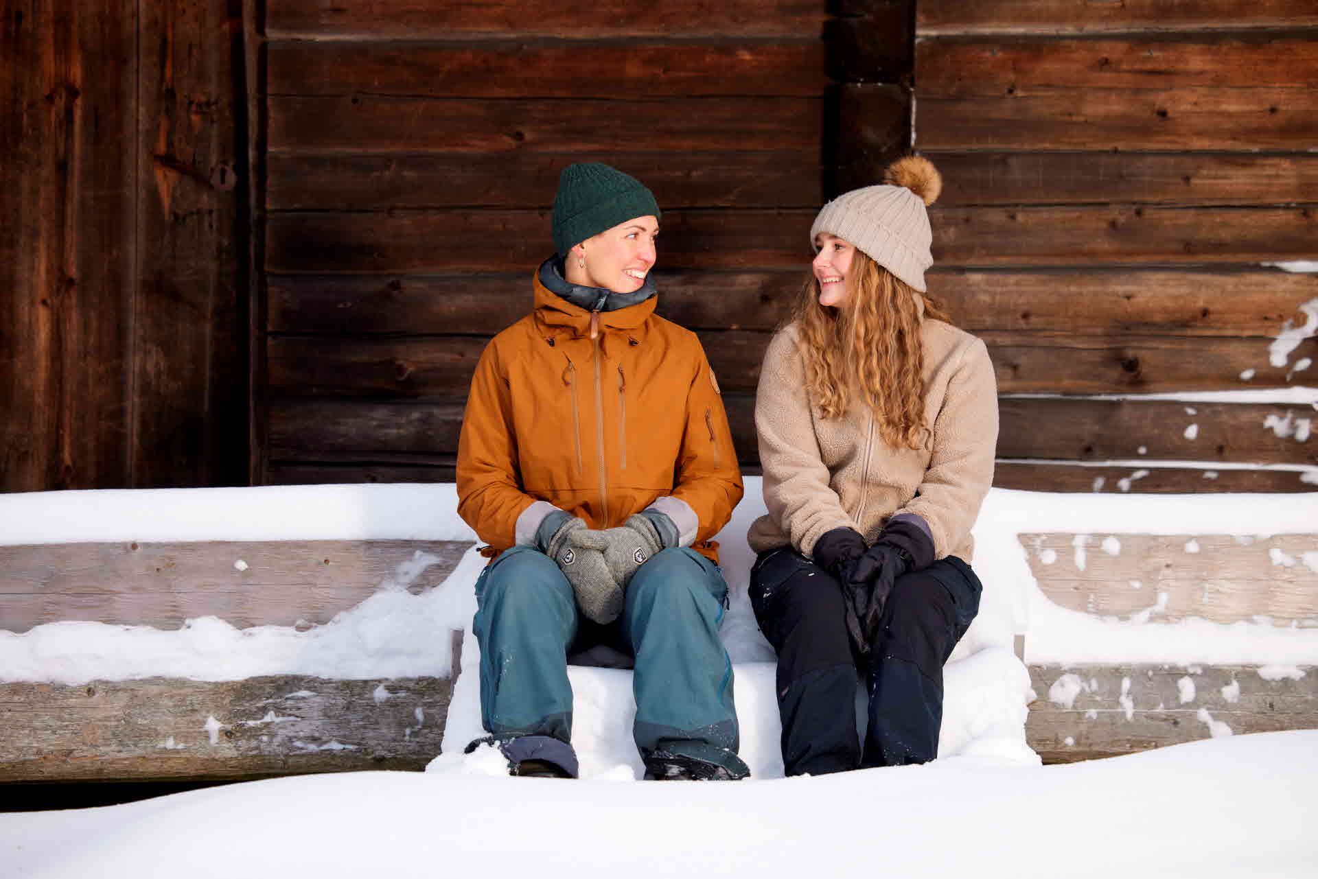 Två tjejer som sitter på en snötäckt bro framför ett hus.