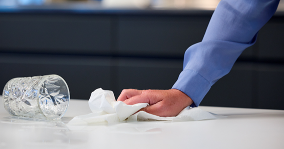 Hand with paper towel wiping up spilled liquid from a glass.