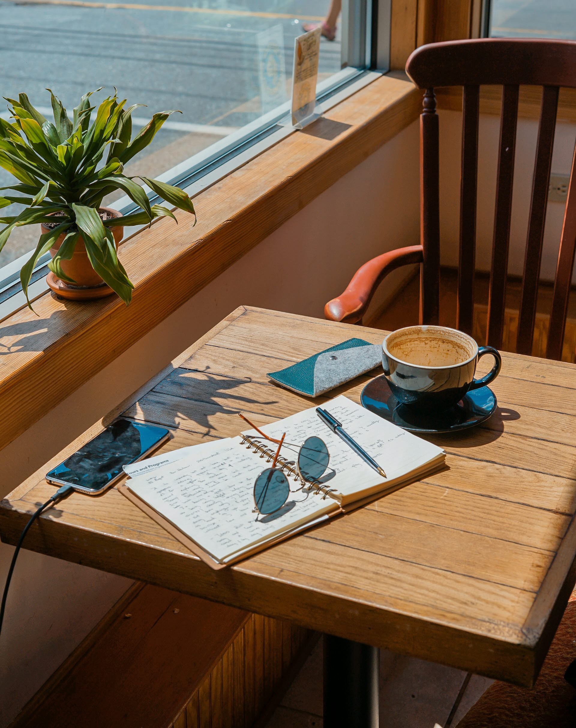 Sittplats i solen vid ett bord med en kopp kaffe, en bok och solglasögon.