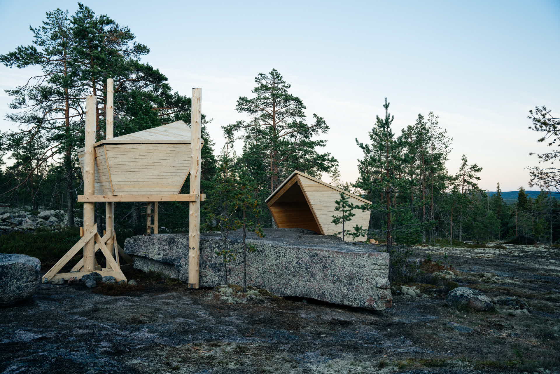 Två vindskydd placerade mitt emot varandra. Mellan vindskydden är ett stort stenblock, skapat av istiden.