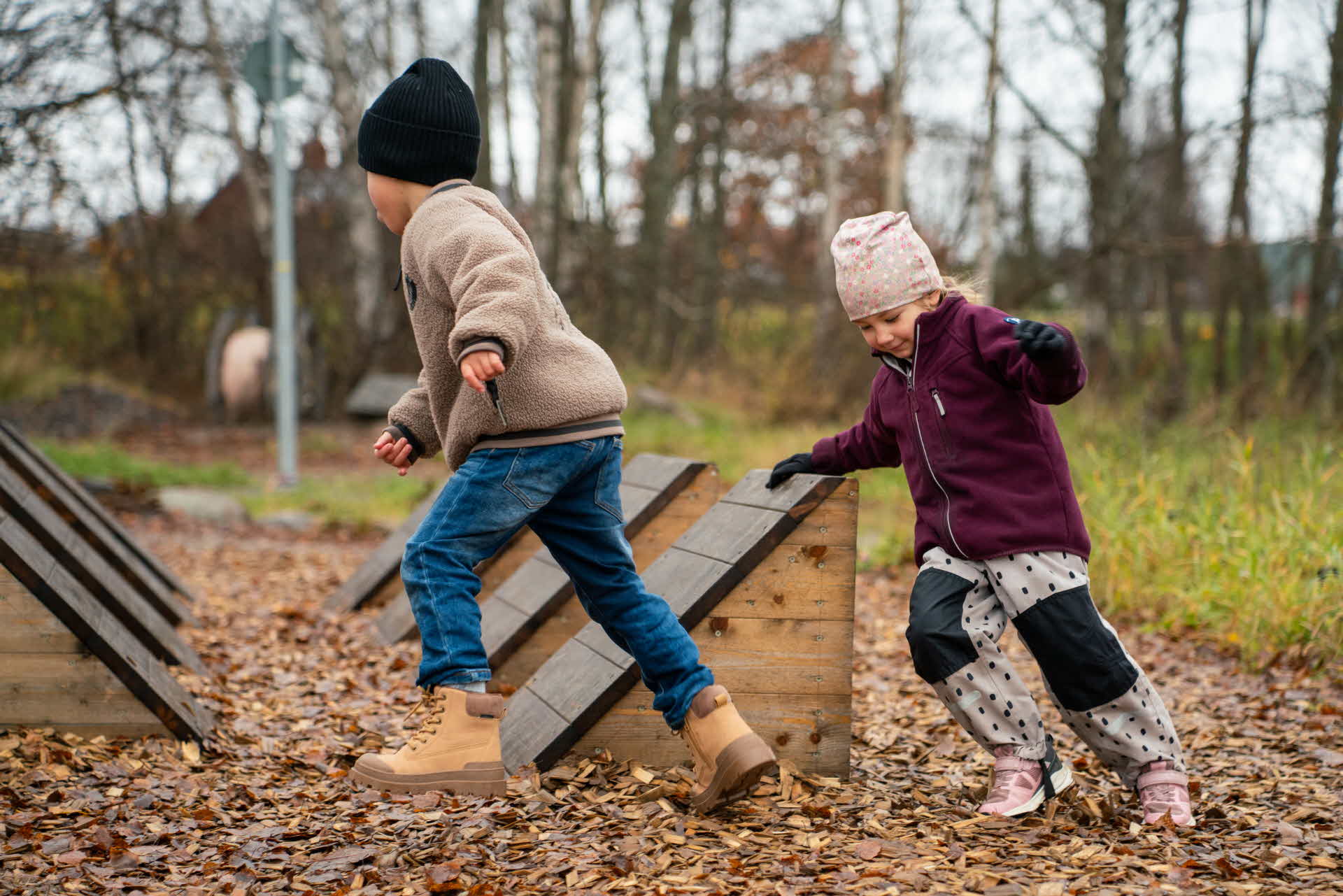 Två barn som springer runt på aktivitetsbanan som är byggd i trä.