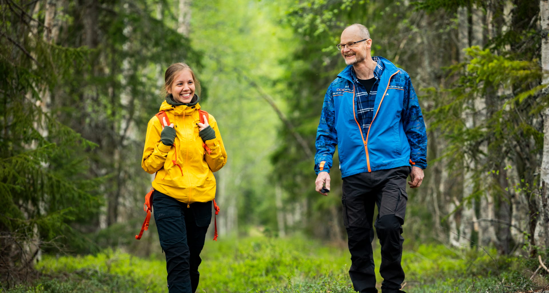 Two people walking in a forest, seen from the front.