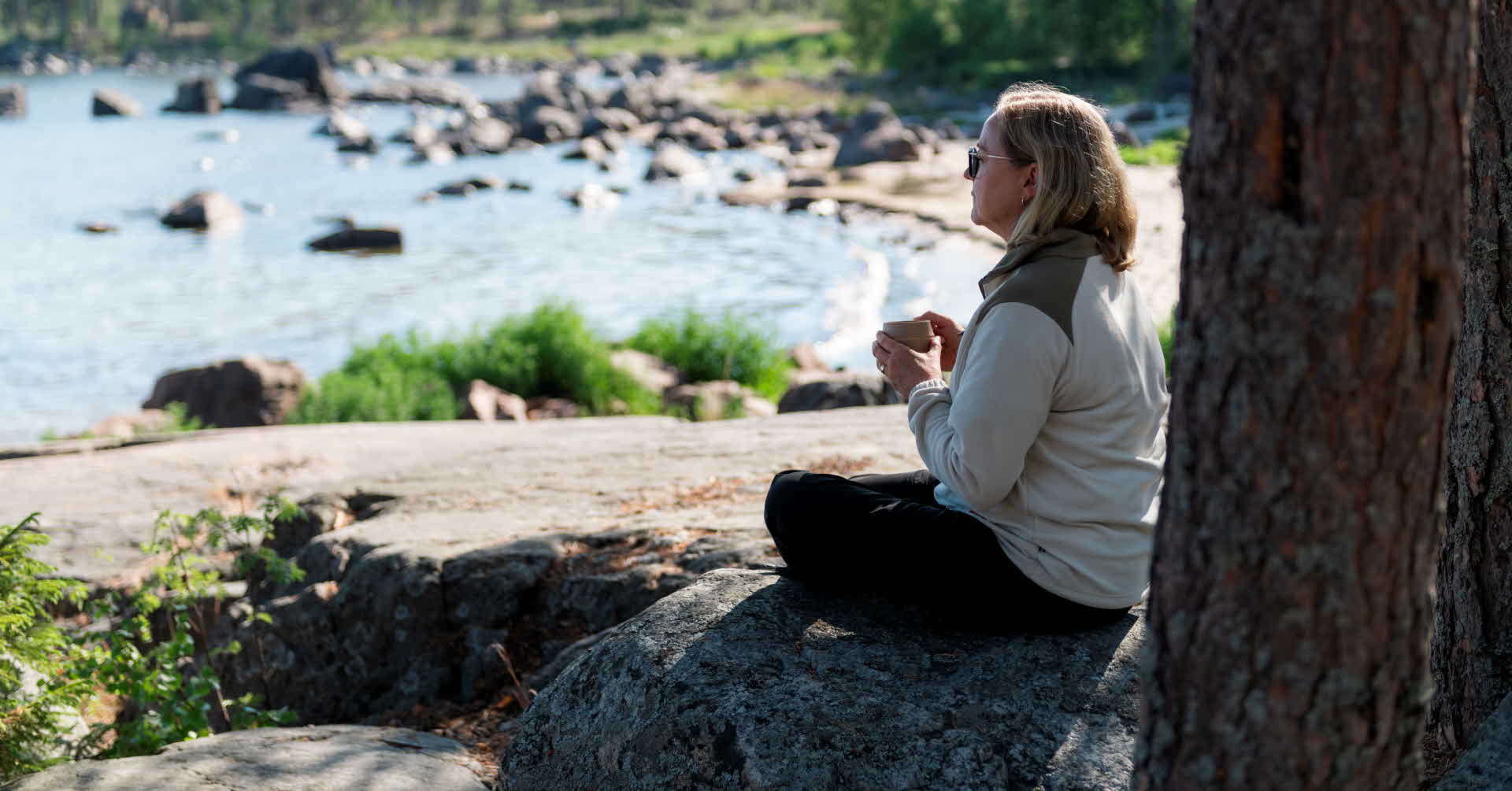 En människa sitter på en klippa och blickar ut över havet.