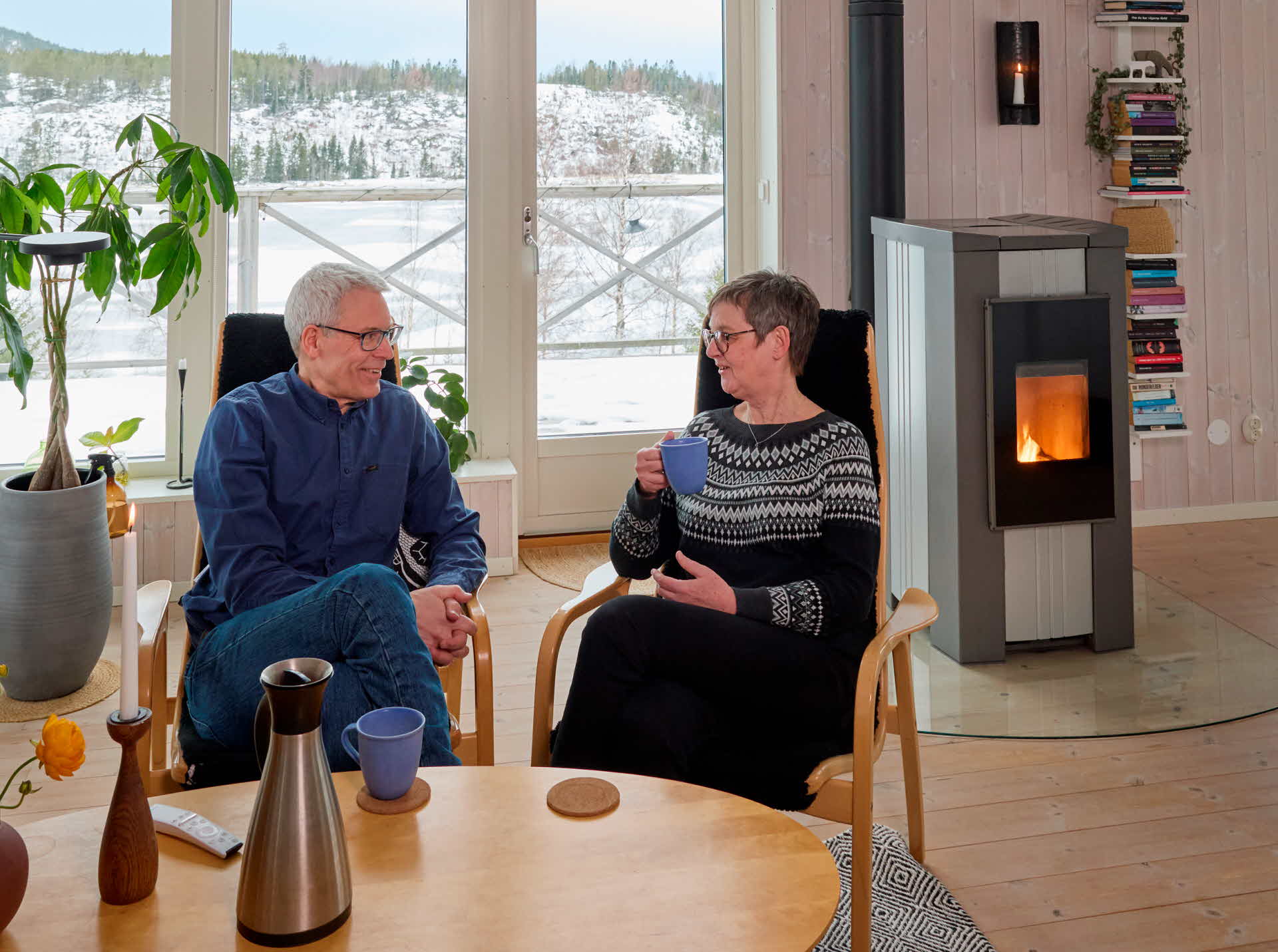 Två personer som sitter i vardagsrummet framför en pelletskamin