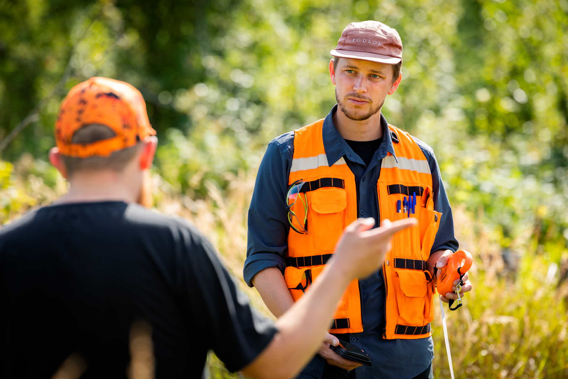 Två personer står i skogen och pratar.