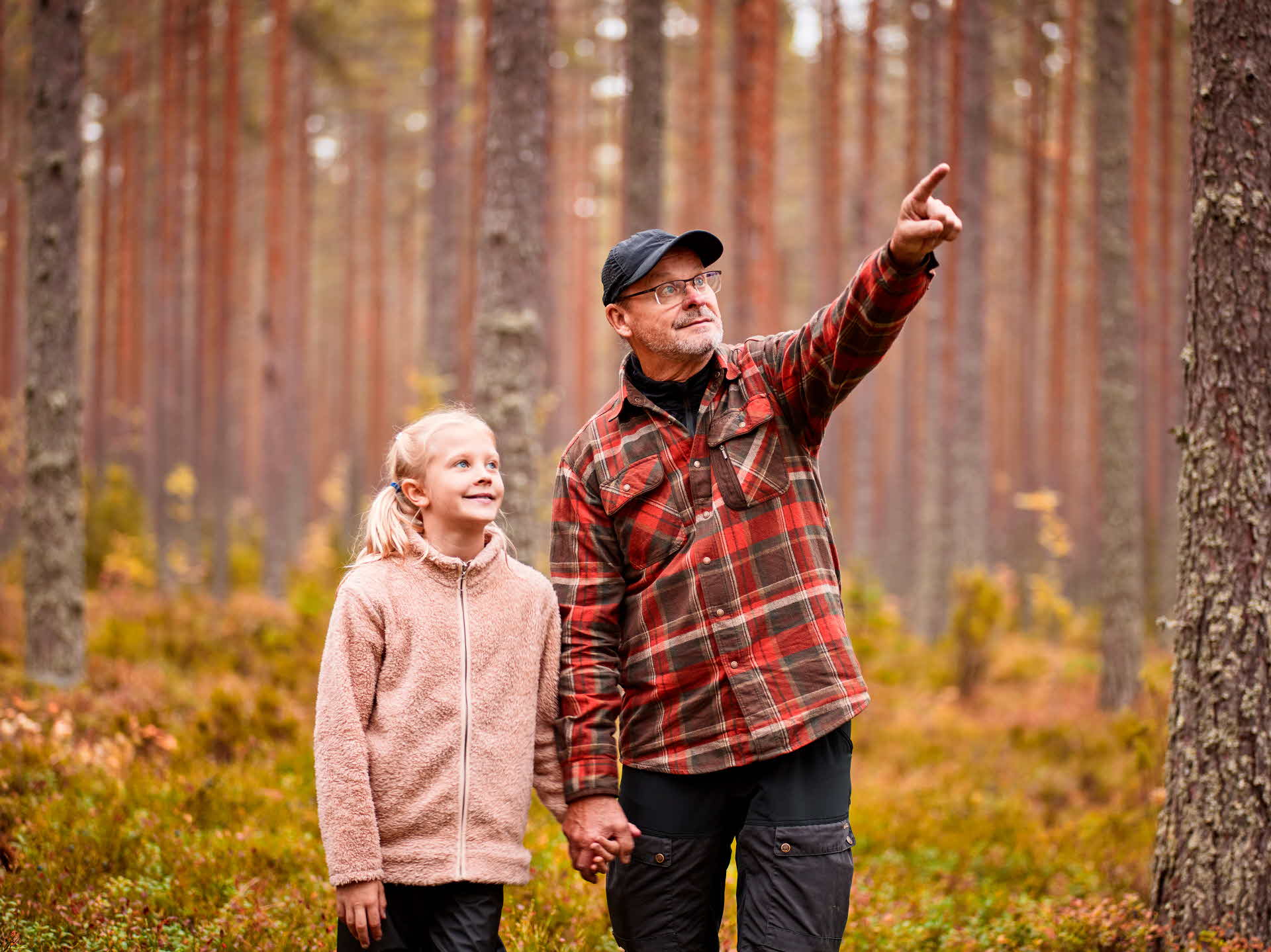 A girl and her grandfather standing in a pine forest.