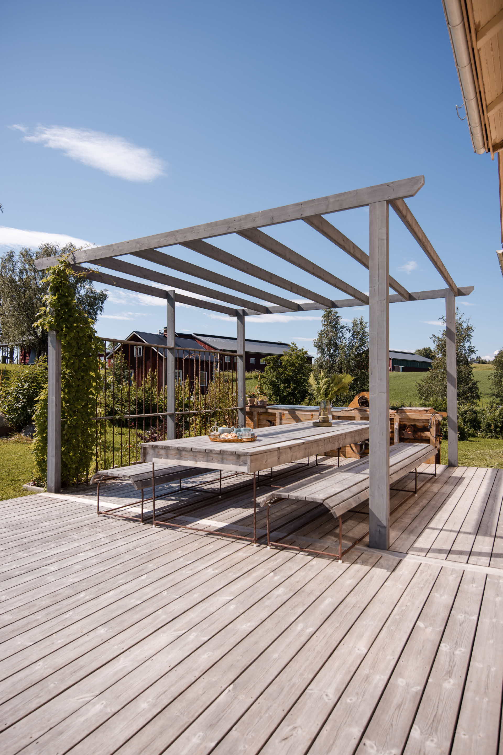 Uteplats med pergola och matplats på en altan vid ett bostadshus.