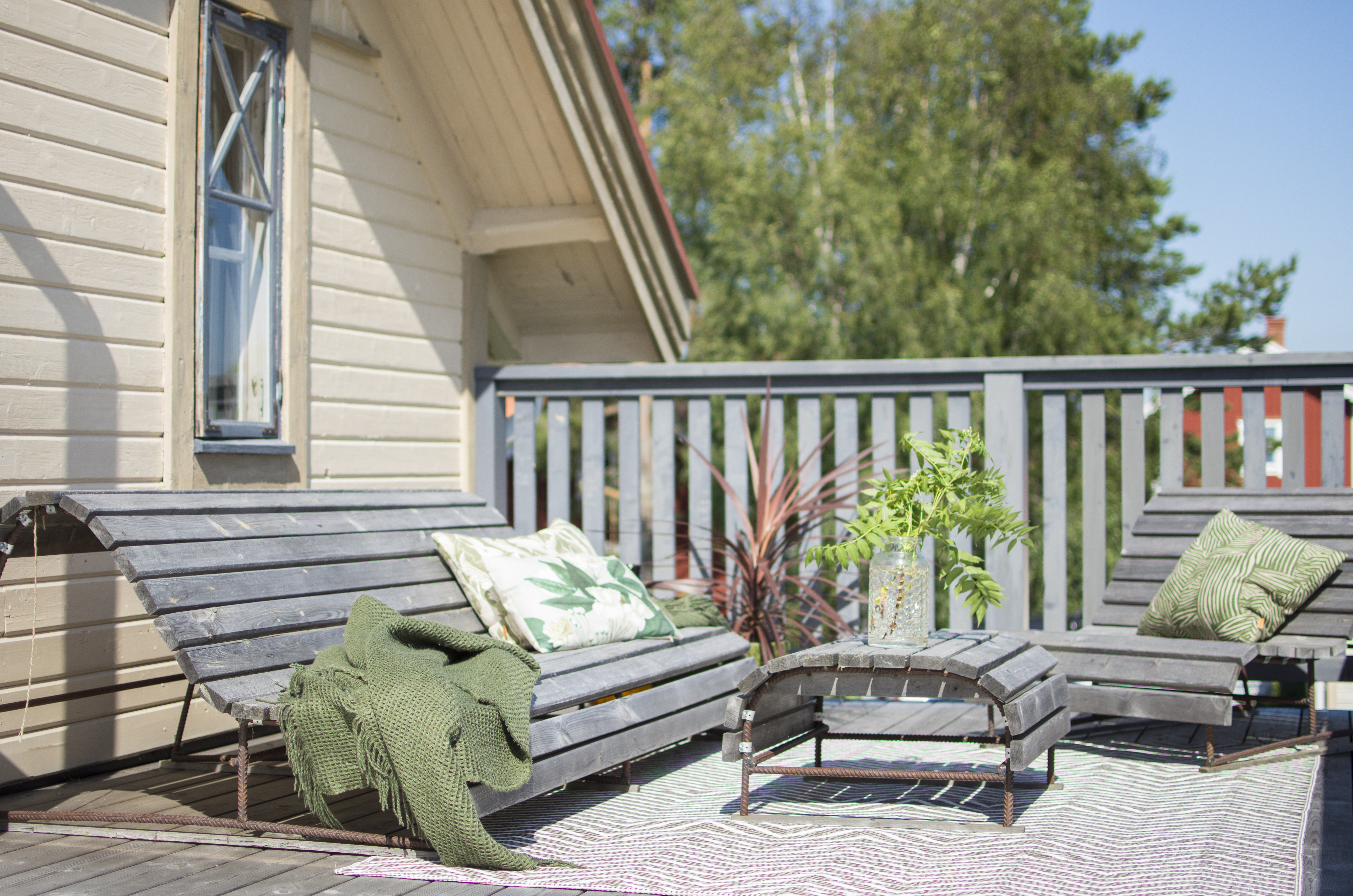 En terrasse med en stor hjemmesnekret sofa i kjernefuru, med tilhørende bord og lenestol, også disse snekret i kjernefuru. På bordet står en blomst, og i sofaen ligger en pute og et pledd.