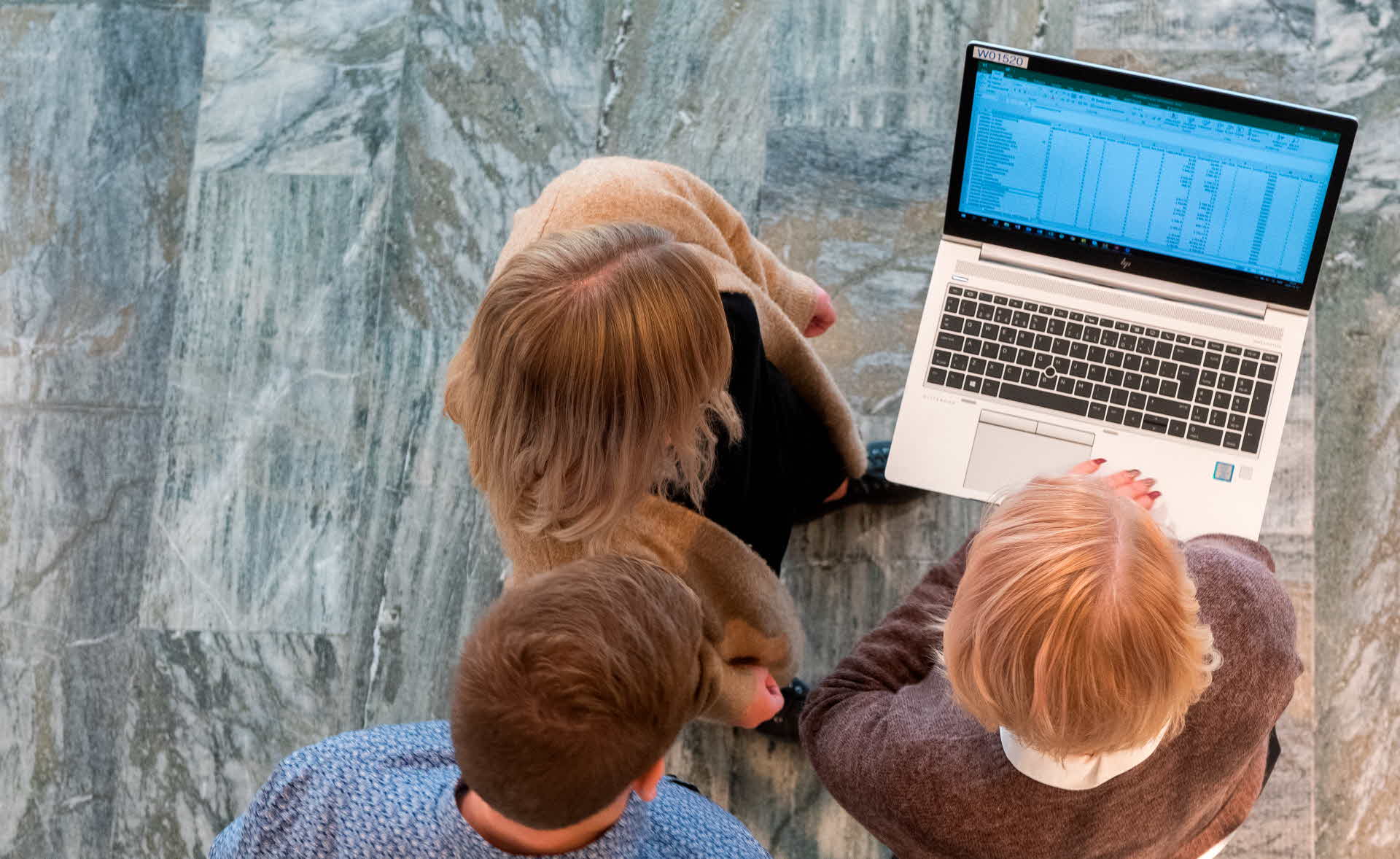 Three people are looking at a laptop.