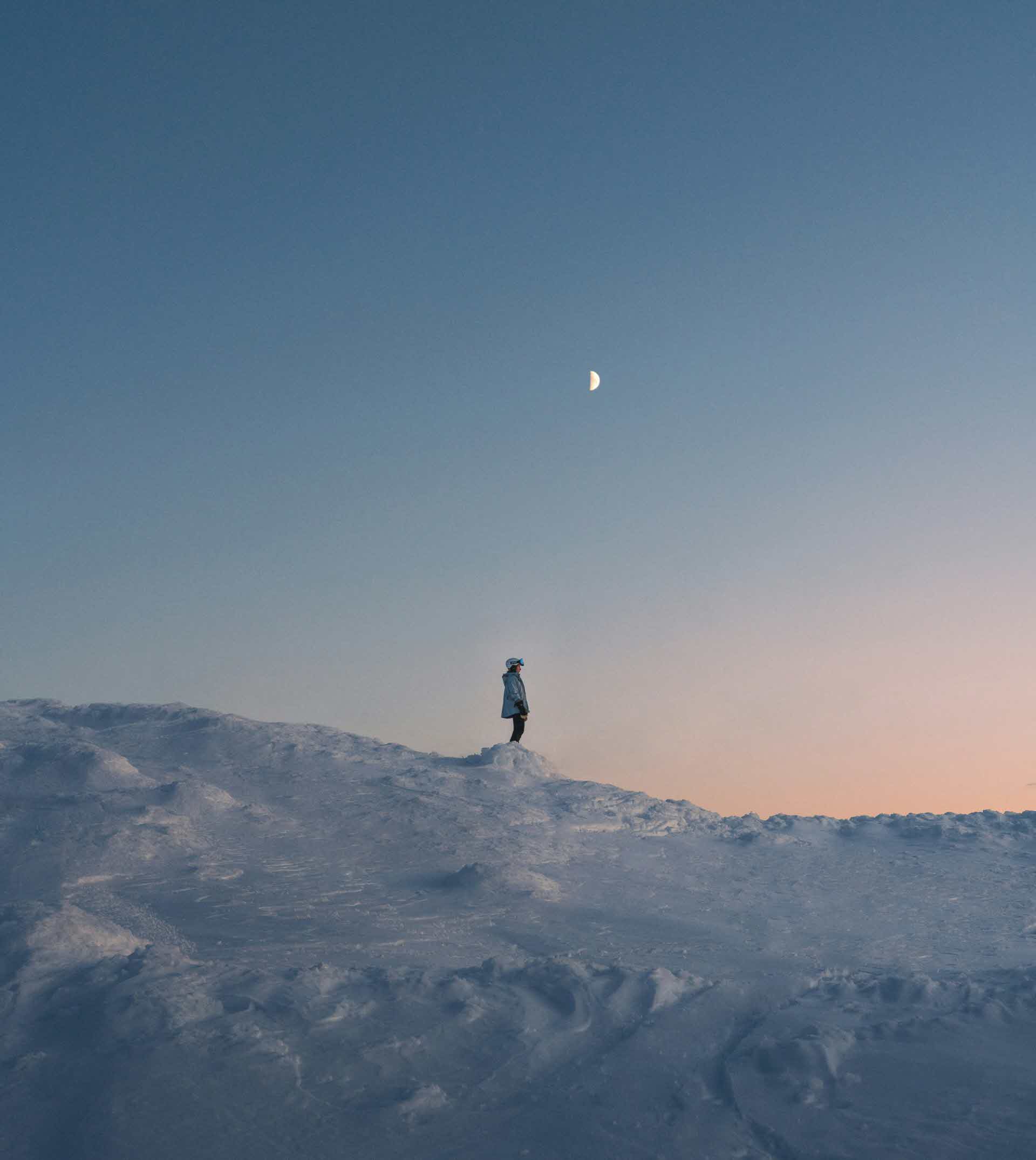 Skidåkare stående i skymningen på en fjälltopp.