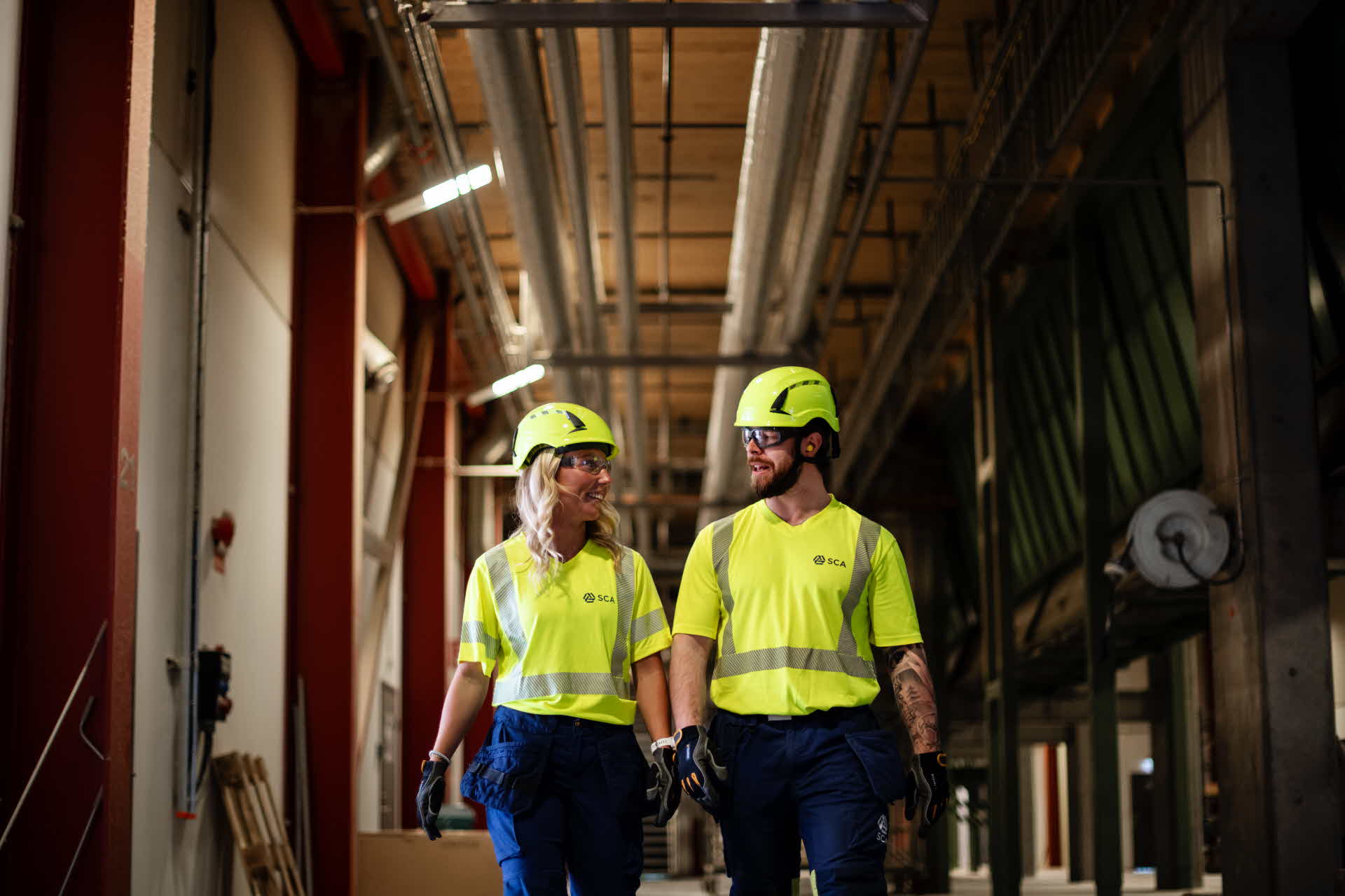En kvinna och en man går bredvid varandra i industrimiljö