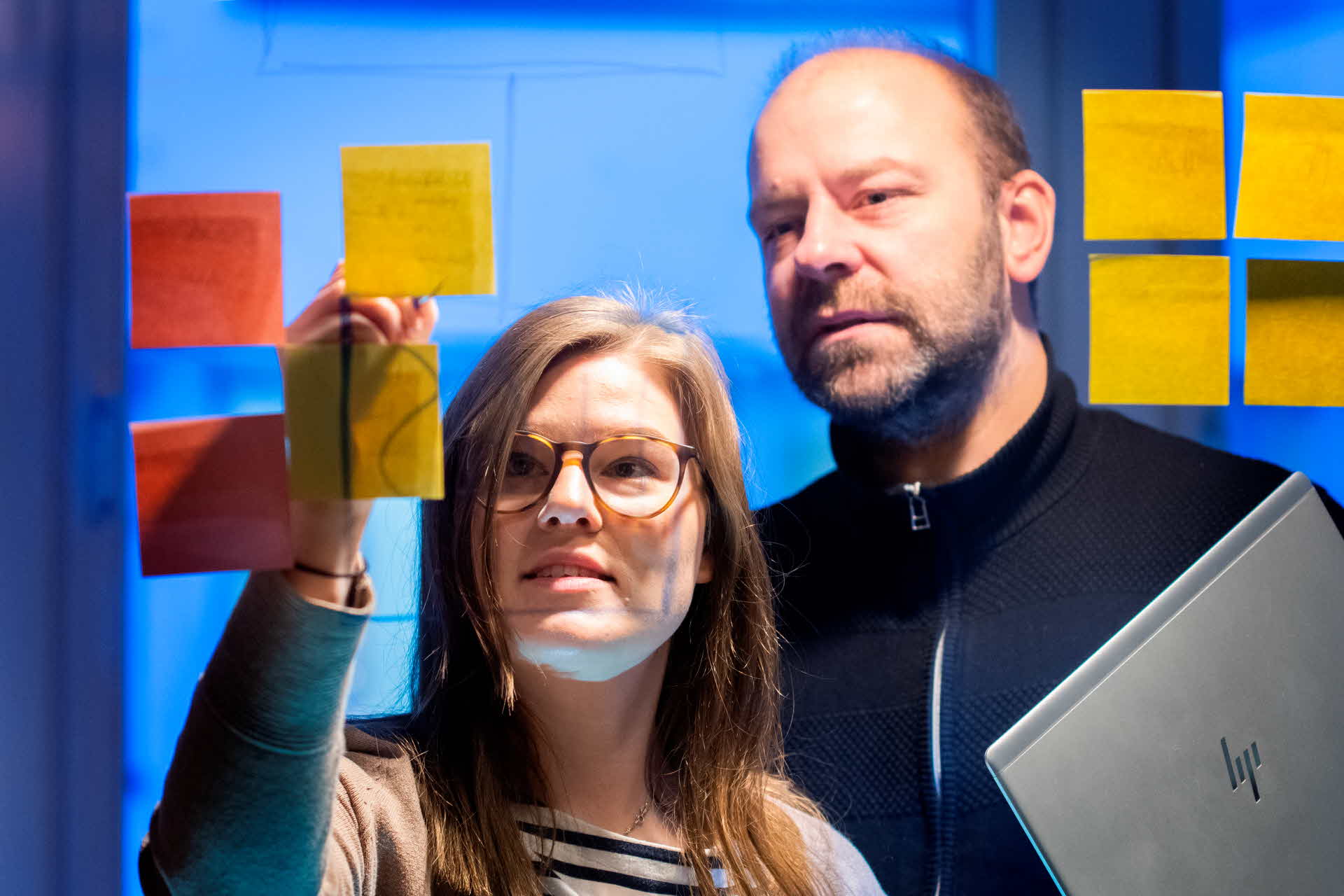 Two employees putting up sticky notes on a wall.