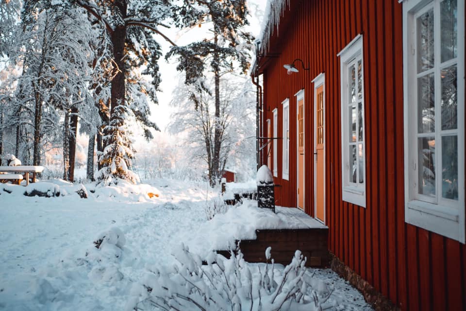 Entré till en röd bruksbyggnad omsluten av snö och skog.