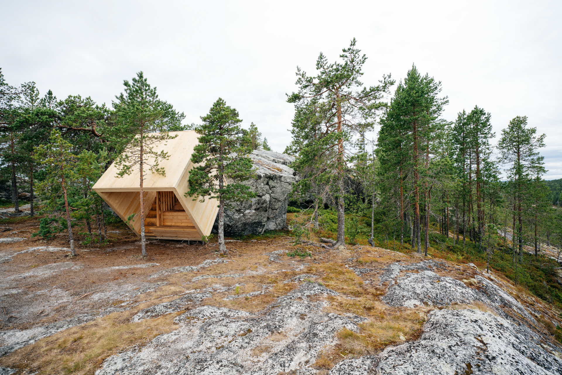 Ett vindskydd format som en kub, lutas med 45 gradig lutning mot ett stenblock.