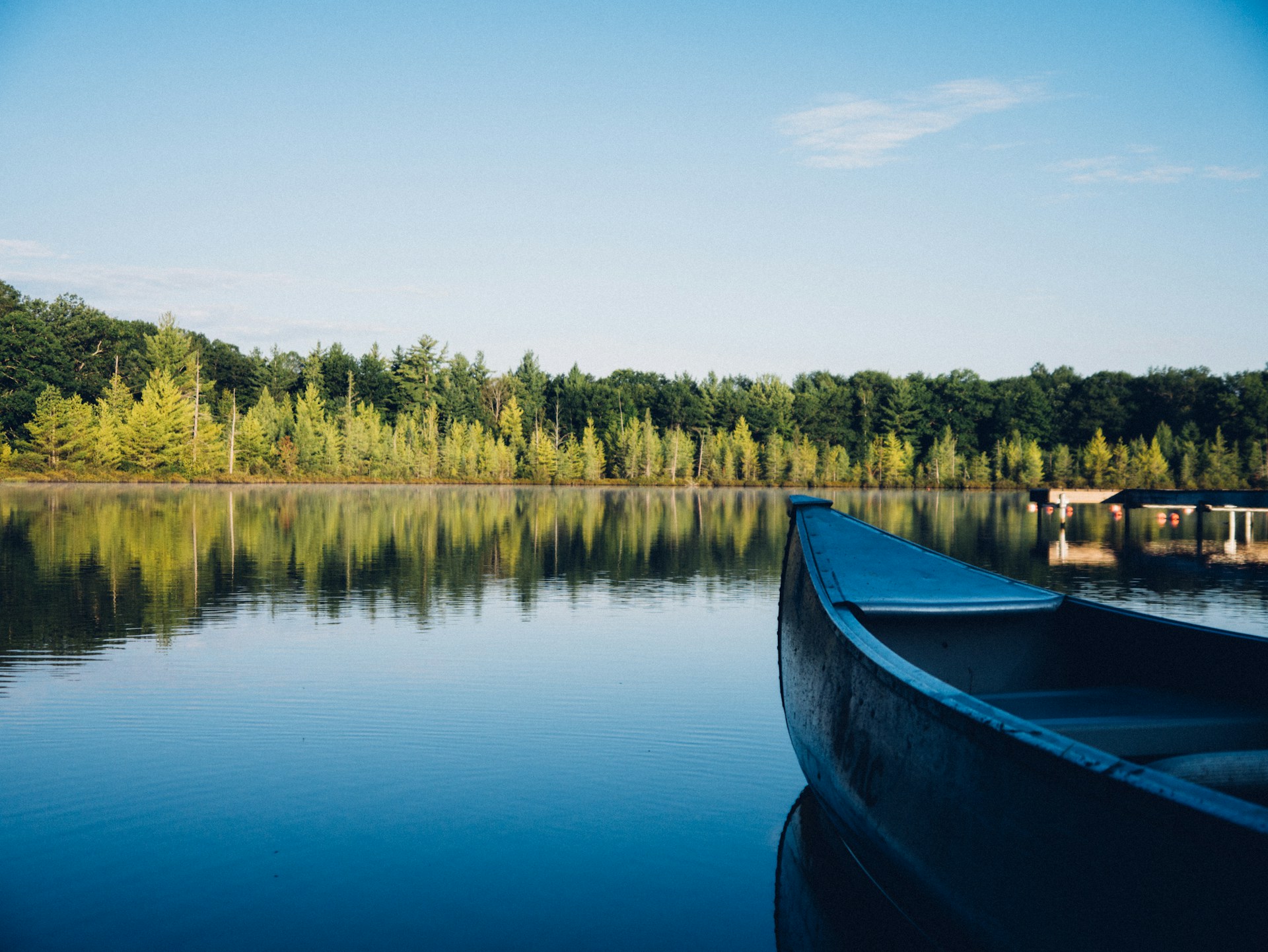 Kanot på spegelblank sjö intill skog.