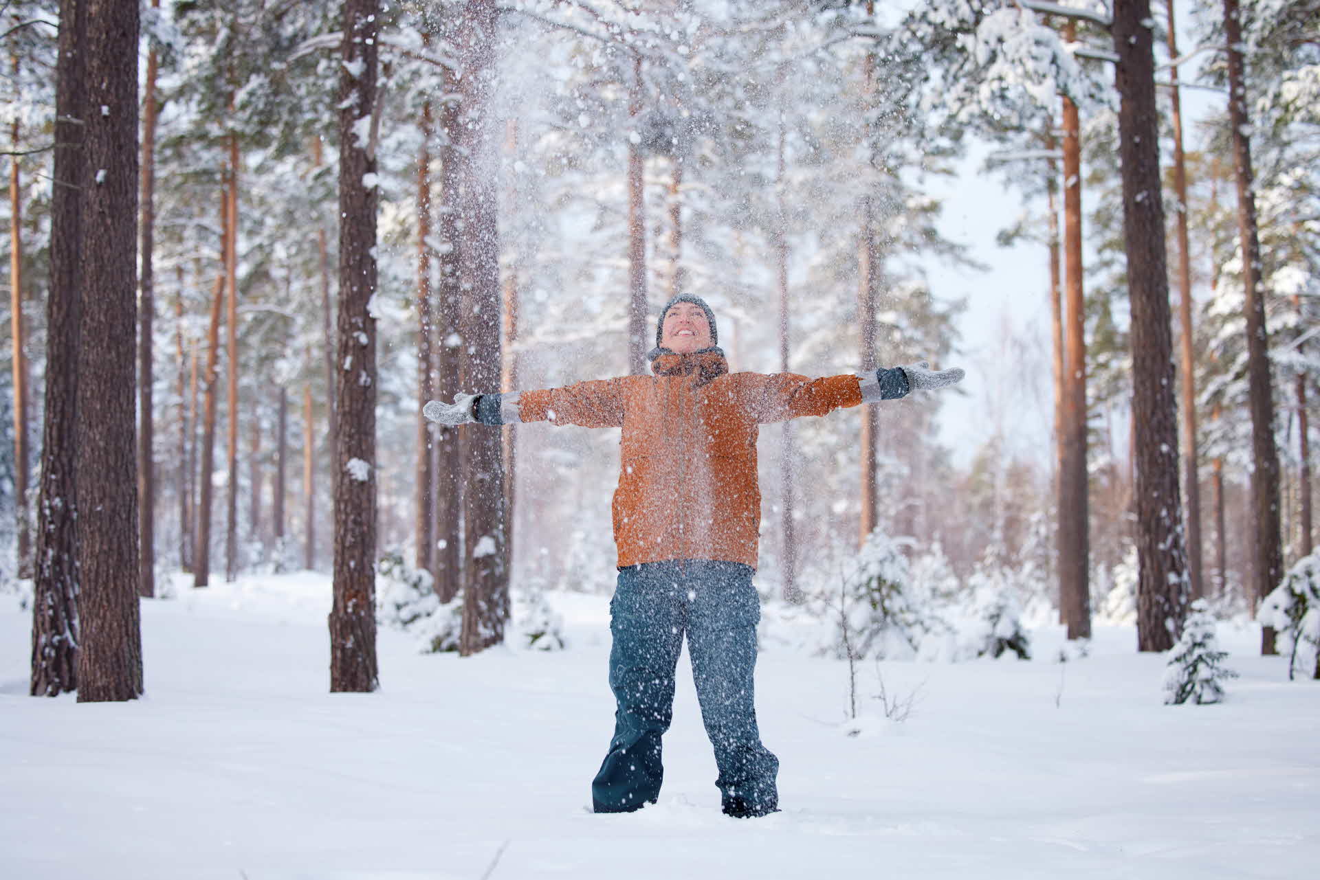 En människa kastar pudersnö ovanför sitt huvud, i en snötäckt skog.