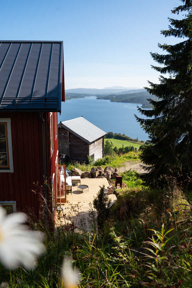 Kortsidan på ett rött hus, men en trall intill, sedd uppifrån med en stor sjö och berg i bakgrunden.
