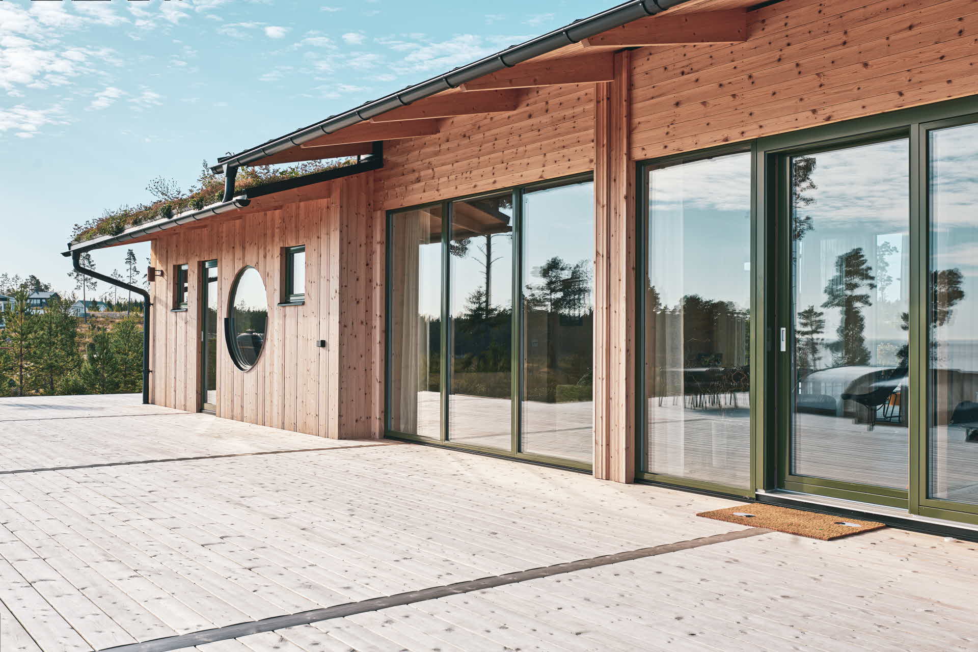 Ett trähus med stora glaspartier och en stor trall i trä.