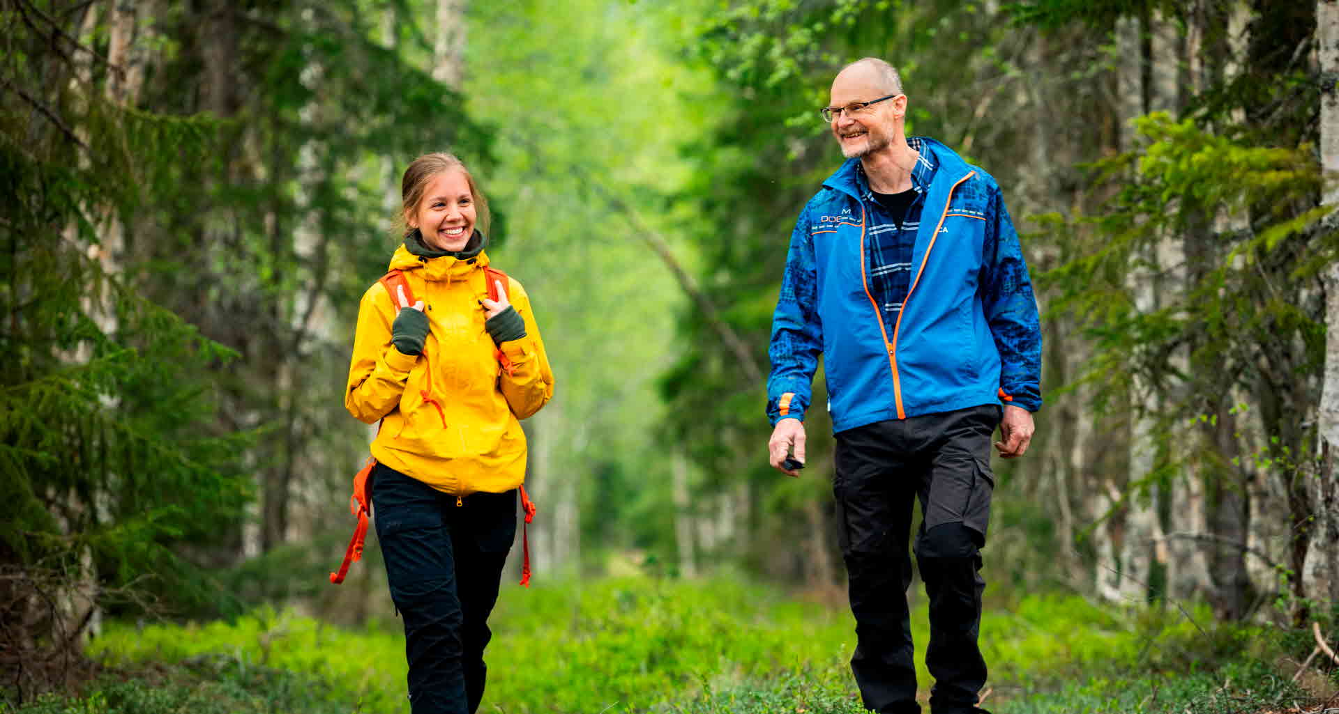 Two people walking in a forest, seen from the front.