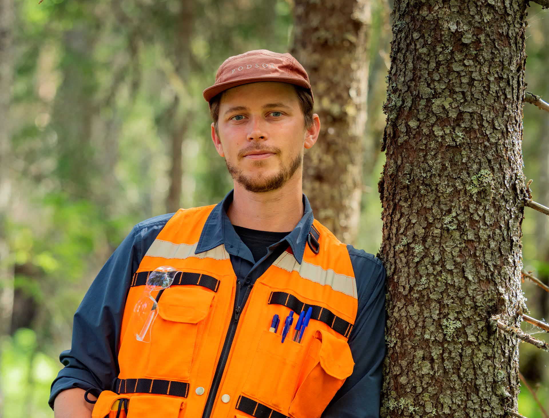 En medarbetare lutar sig mot ett träd i skogen.