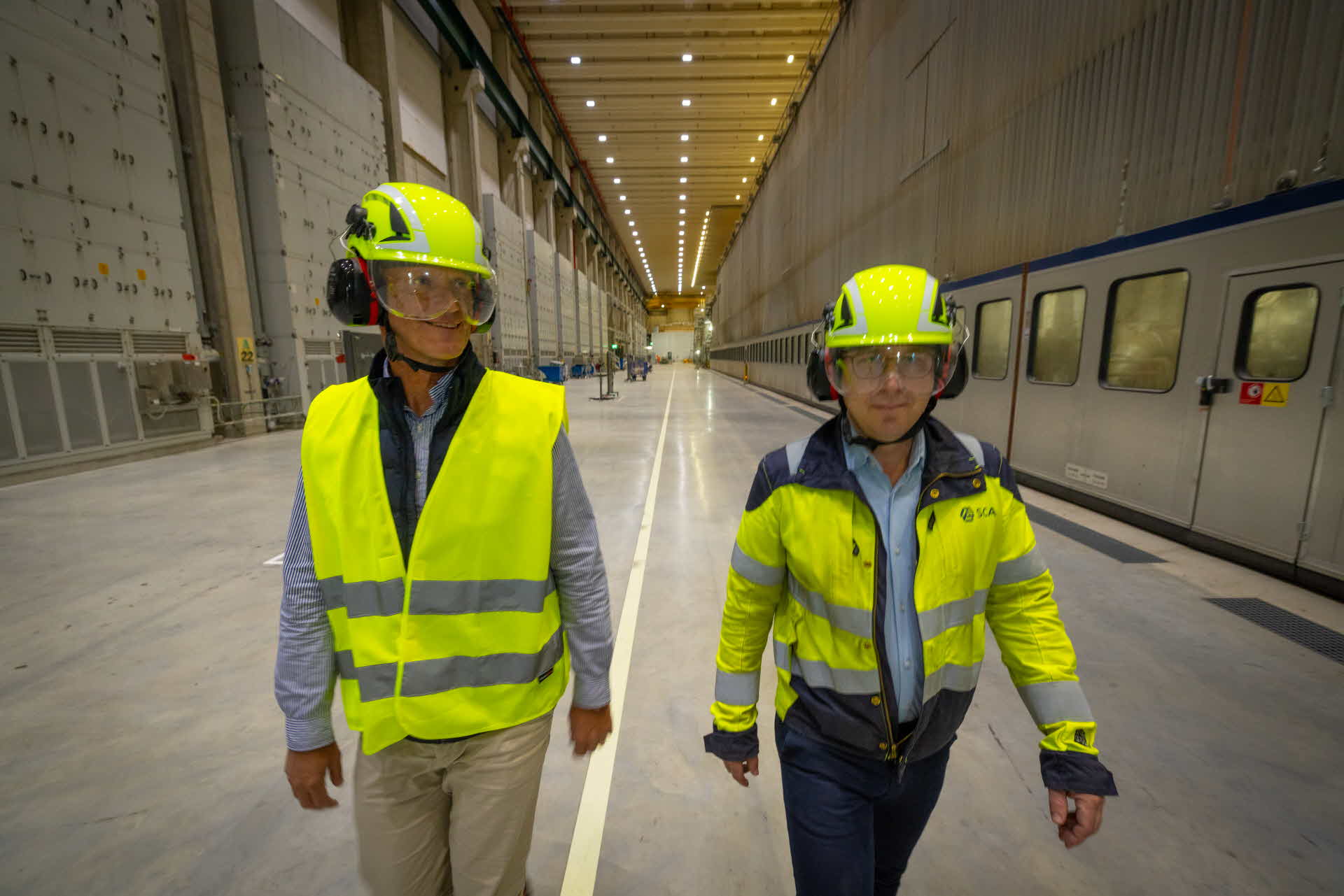 Two men in helmets and high-visibility clothing walking inside a paper mill