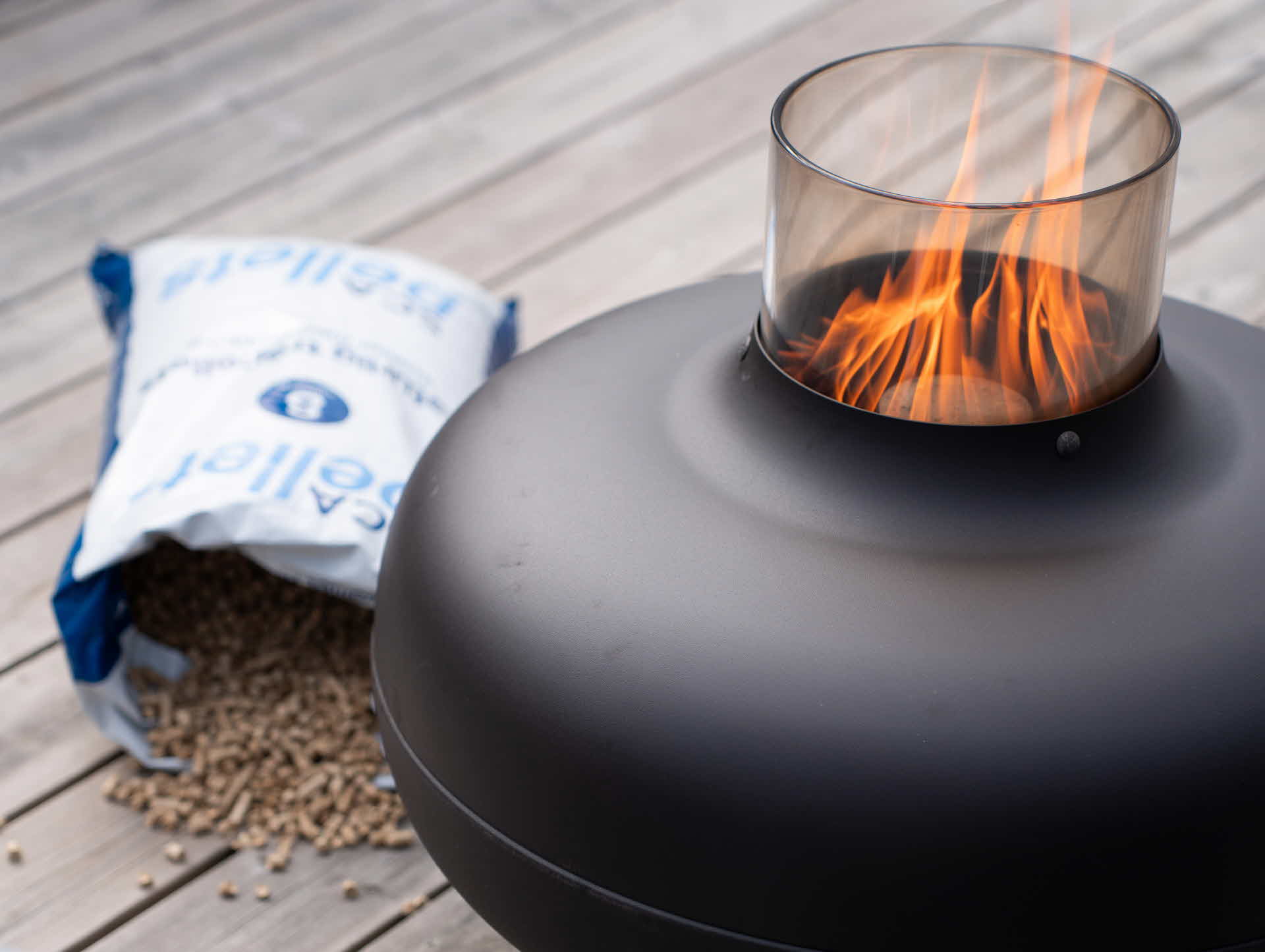 Öppnad pelletssäck på trätrall med en terassvärmare som brinner med pellets