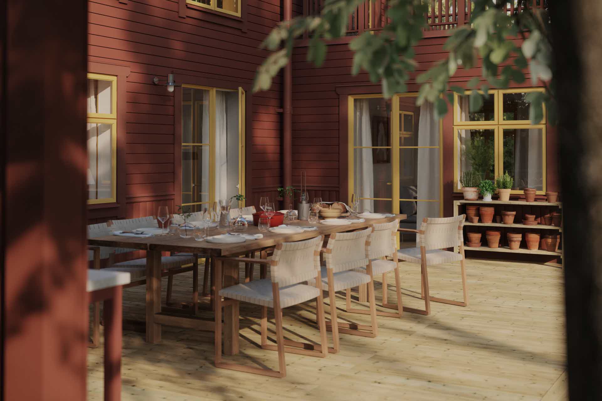 Ett rödmålat hus med en stor trall framför. På trallen står ett stort bord med åtta stolar runt omkring.